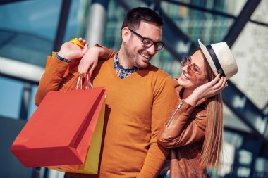 Çift alışveriş çantaları taşıyor ve şehirde yürürken gülümsüyor.