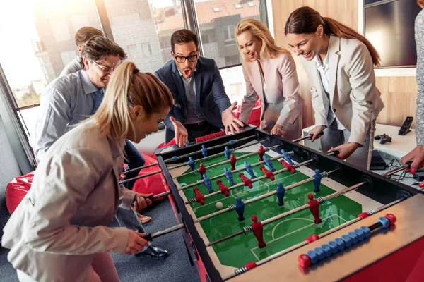 Business people having great time together. Colleagues playing table football in modern office.