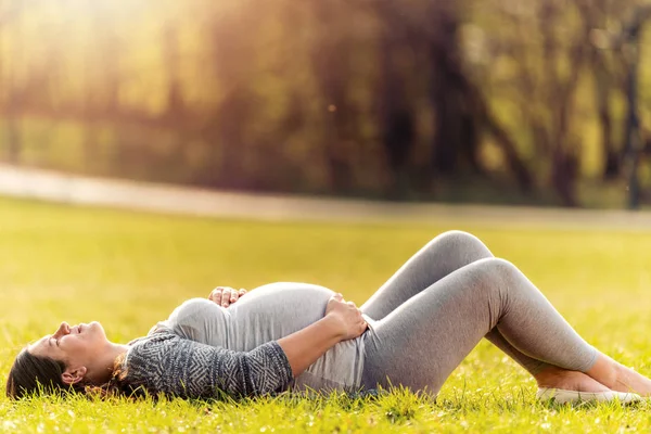 美丽的孕妇躺在草地上在阳光明媚的日子 — 图库照片