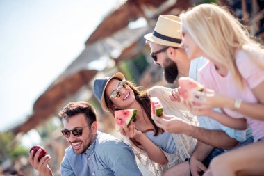 Bir grup arkadaş eğleniyor, sahilde karpuz yiyor. Yaz konsepti.