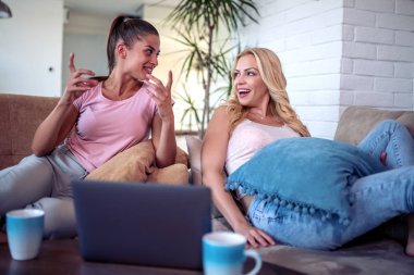 Mutlu genç kadın arkadaşlar evde dizüstü bilgisayar kullanarak ve kahve içmek.