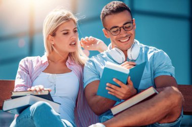 Mutlu genç çift gülümseyerek ve açık havada bir kitap okuyor. Üniversite hayatının tadını çıkarıyorlar..