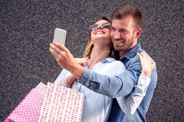 Alışveriş torbalı mutlu çift akıllı telefonlu selfie çekiyor..