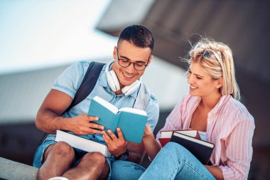 Mutlu genç çift gülümseyerek ve açık havada bir kitap okuyor. Üniversite hayatının tadını çıkarıyorlar..
