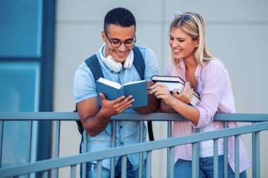 Mutlu genç çift gülümseyerek ve açık havada bir kitap okuyor. Üniversite hayatının tadını çıkarıyorlar..