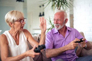 Mutlu yaşlı çift oturma odasında birlikte oturan ve bir video oyunu oynarken gülüyor.