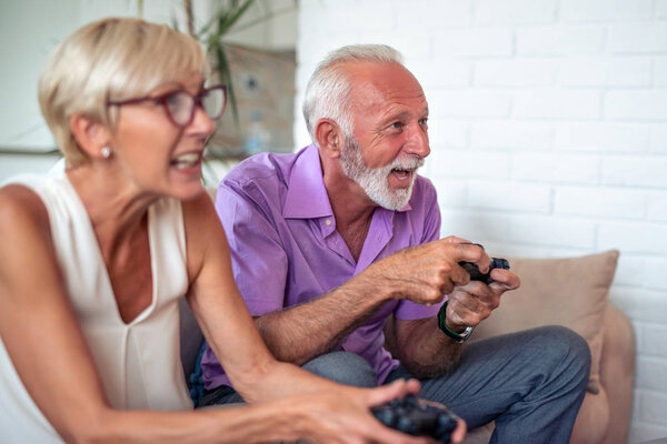 Happy senior couple sitting together in their living room and laughing while playing a video game.