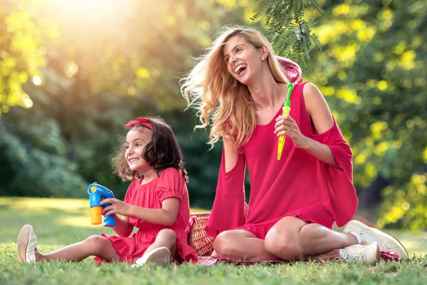 美しいお母さんと娘が夏の公園でシャボン玉を吹いて — ストック写真