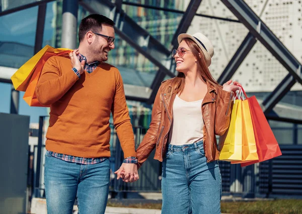 这对年轻漂亮的夫妇带着购物袋走在街上 面带微笑 — 图库照片