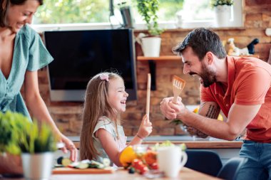 Yemek, yemek ve ev konsepti. Anne, baba ve çocuk mutfakta salata yapmak için sebze kesiyorlar..