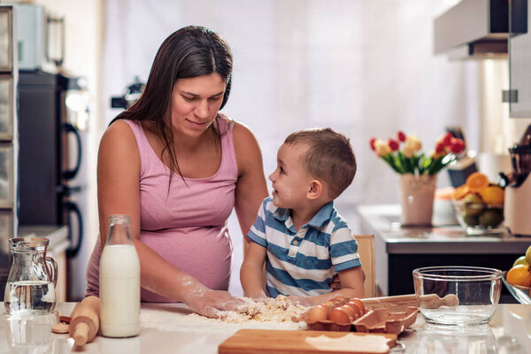 Беременная мать и ее сын наслаждаются на кухне и пекут печенье.
