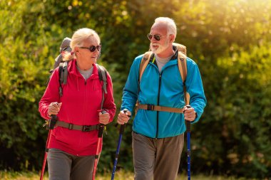 Senior couple walking in nature with backpacks.Nature,leisure time and lifestyle concept. clipart