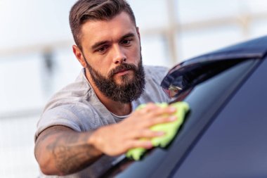 Genç adam arabasının bagajını lifli bezle cilalıyor. Yıkama, yaşam tarzı ve insanlar konsepti.