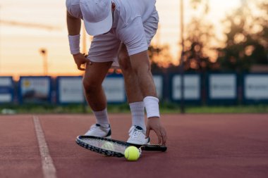 Close up view of man, tennis racket and balls on the tennis court.