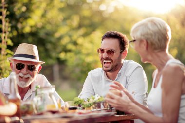 Mutlu bir aile güneşli bir günde bahçede yemek yiyor..