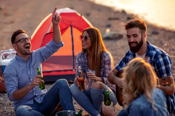 Group of excited friends having fun together on the beach, drinking beers.