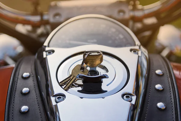 Control panel of classic orange motorcycle with lots of chrome parts and riveted tie, made of genuine brown leather. Keys are in ignition lock Motorcycle is shot at sunset in park