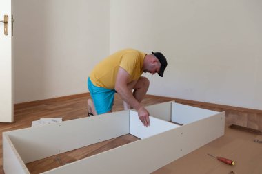 Yeni evde sıradan giyinmiş mobilya montajı yapan bir adam. Marangoz evde mobilya onarıp monte ediyor.