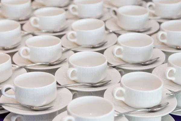 Righe di caffè bianco pulito o tazze da tè, piatto e cucchiaio in una caffetteria o ristorante pronto a servire una bevanda calda — Foto Stock