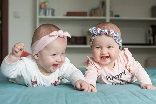 Gêmeos adoráveis bebê se divertindo na cama em casa. Miúdos bonitos com penteados (fitas), sorrindo, rindo. Conceito de felicidade . — Fotografia de Stock