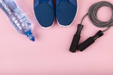 Mavi spor ayakkabılar, ip atlama ve pembe arka plan üzerinde su şişesi. Sağlıklı yaşam salkı kavramı, günlük eğitim ve irade gücü