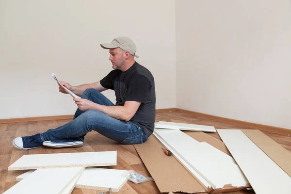 Homem lendo instruções de montagem para móveis em casa nova. Reparação de carpinteiro e montagem de móveis em casa — Fotografia de Stock