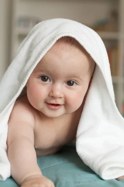 Kleine baby glimlachend, lachend.Leuke baby liggend op haar buik over een witte handdoek. — Stockfoto