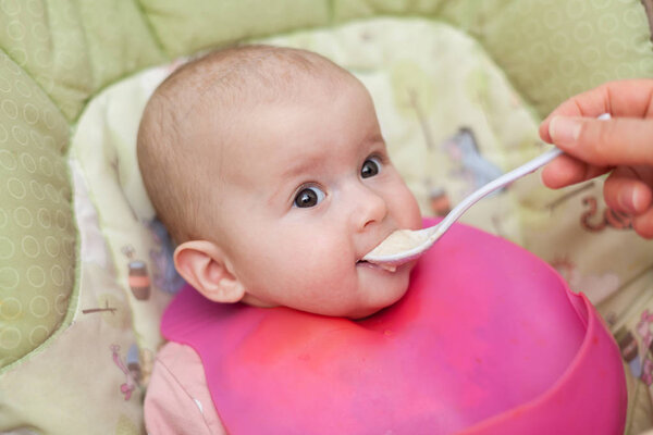 mother gives baby food from a baby spoon. baby eating food first time. weaning baby 
