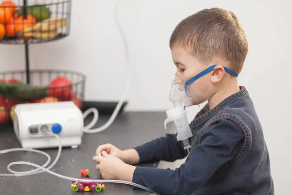 Menino brincando com brinquedos ao fazer sua inalação com nebulizador em casa. Criança asma inalação nebulizador vapor conceito tosse doente . — Fotografia de Stock