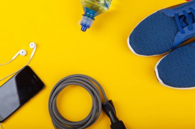 Spor ayakkabılar, ip atlama, sarı arka planda kulaklıklı cep telefonu. Üst Manzara. Fitness, spor ve sağlıklı yaşam tarzı kavramı.