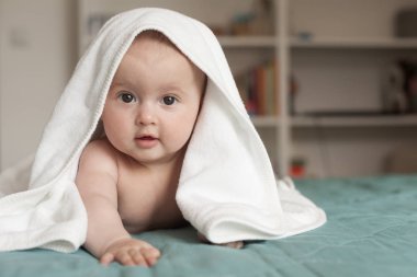 Küçük bebek gülümsüyor. Sevimli bebek beyaz bir havlu üzerinde karnının üzerinde yatan.