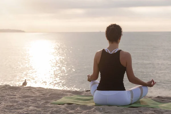 Жінка розслабляється в позі лотоса на пляжі. Медитація біля моря на сході сонця . — стокове фото