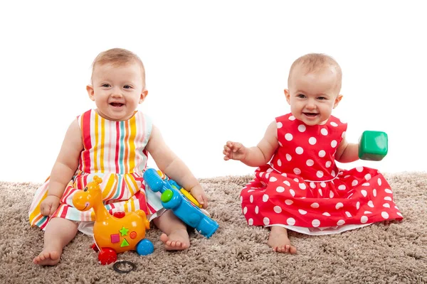 Twee schattige baby meisjes spelen met speelgoed thuis, geïsoleerd op wit — Stockfoto