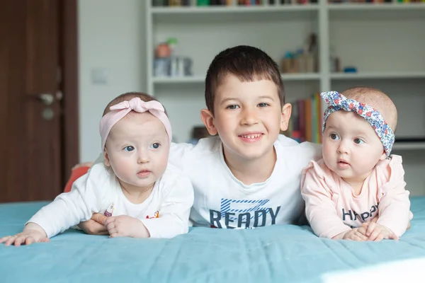 Hermanos y hermanas yacen en la cama y sonríen. Hermano abrazó a sus hermanitas gemelas. Son muy felices el uno con el otro — Foto de Stock