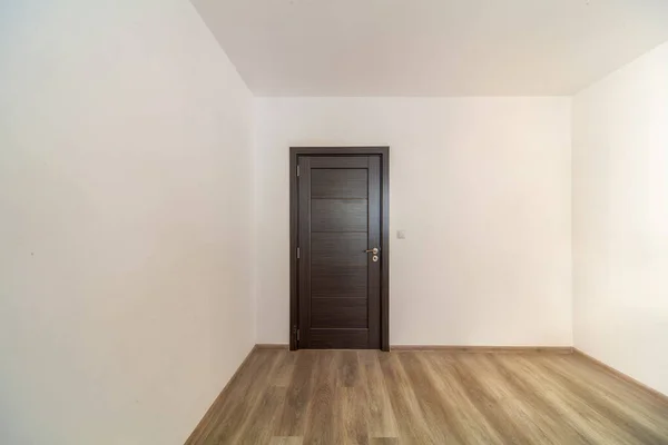 Gesloten houten deur in lege kamer, houten vloer. Witte muren — Stockfoto