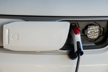 Elektrikli araba aküsünü şarj et. Şarj istasyonunda elektrik kablosu takılı elektrikli araba.