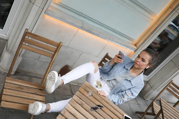 Привлекательная девушка сидит в уличном кафе и пользуется смартфоном . — стоковое фото