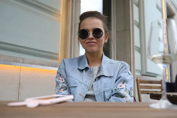 Cheerful girl in sunglasses sits at a table in a street cafe. — Stock Photo, Image