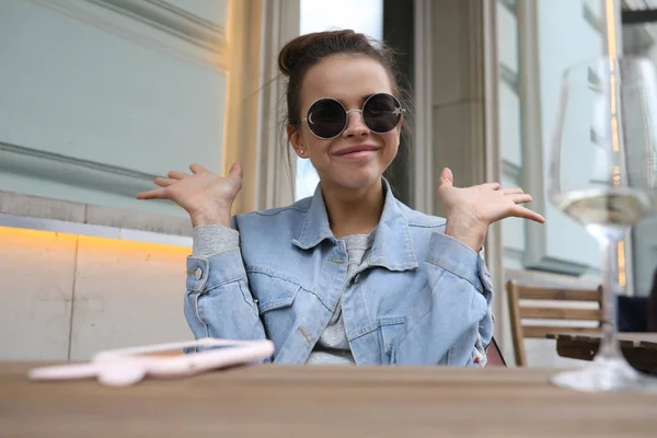 Cheerful girl in sunglasses sits at a table in a street cafe. — Stock Photo, Image