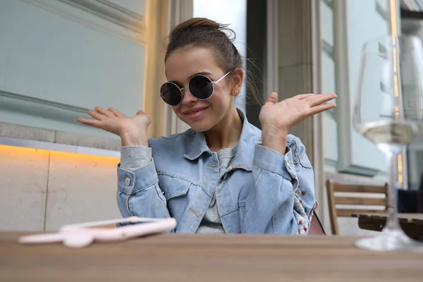 Cheerful girl in sunglasses sits at a table in a street cafe. — Stock Photo, Image