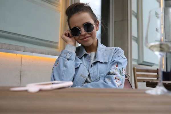 Cheerful girl in sunglasses sits at a table in a street cafe. — Stock Photo, Image