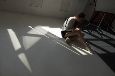 Model yere oturur ve bir profesyonel fotoğraf stüdyosunda bir akıllı telefon kullanır.