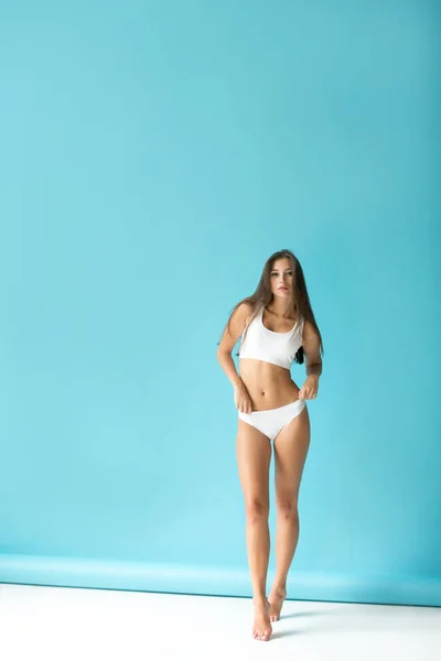 Attraktive junge Frau in weißer Sportunterwäsche auf blauem Hintergrund. — Stockfoto