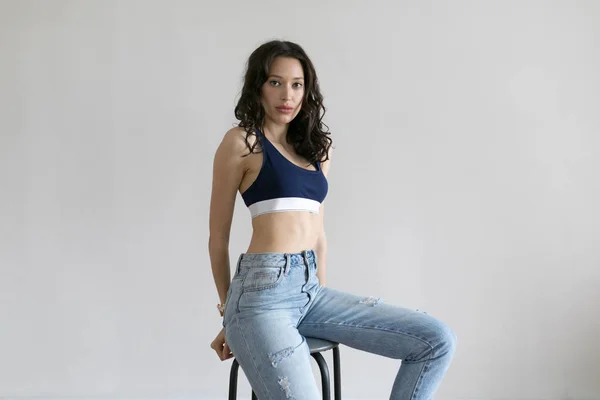 Atraktivní žena v sportovní top a džíny pózy na bílém pozadí. — Stock fotografie