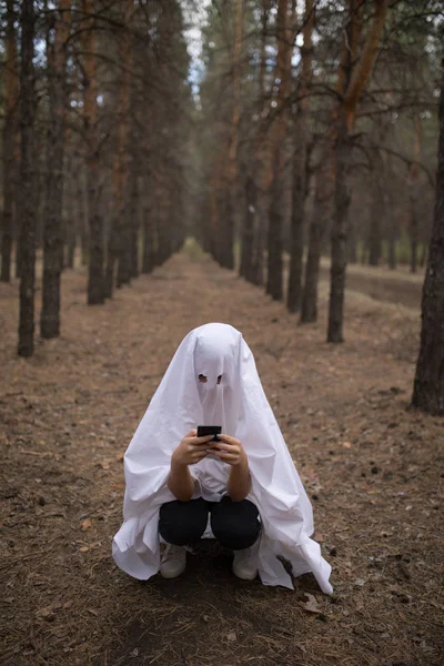 Kvinna i halloween ghost kostym med smartphone i skogen. — Stockfoto