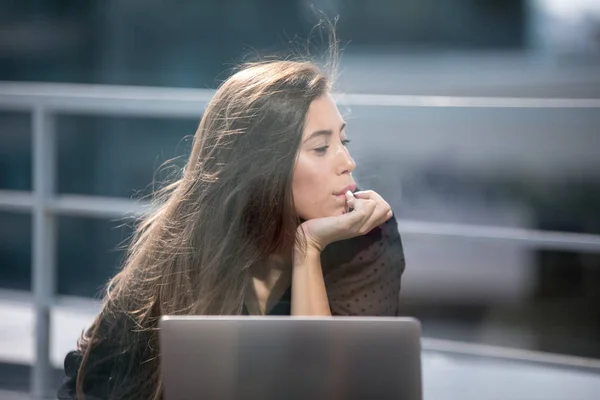 Νεαρή γυναίκα κάθεται στην βεράντα με θέα στην πόλη και χρησιμοποιεί ένα φορητό υπολογιστή. — Φωτογραφία Αρχείου