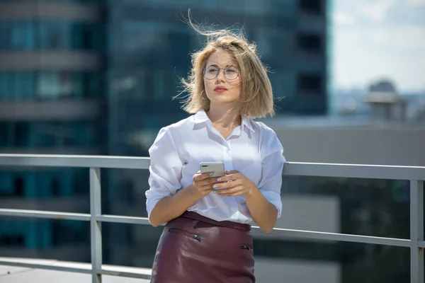 Beautiful business woman uses a smartphone while standing on a city background. — Stock Photo, Image