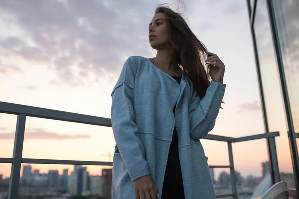 Attractive young woman stands against city and sunset. — Stock Photo, Image