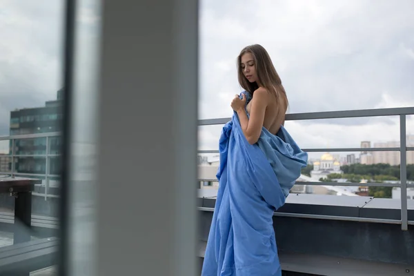 Ragazza nuda avvolta in una coperta si trova sulla terrazza con vista sulla città . — Foto Stock