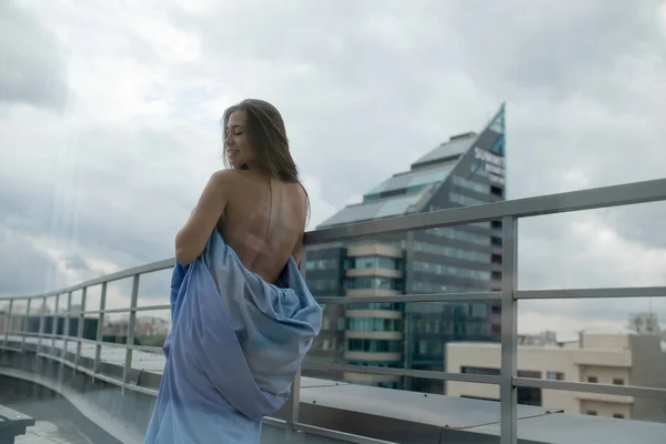 Ragazza nuda avvolta in una coperta si trova sulla terrazza con vista sulla città . — Foto Stock